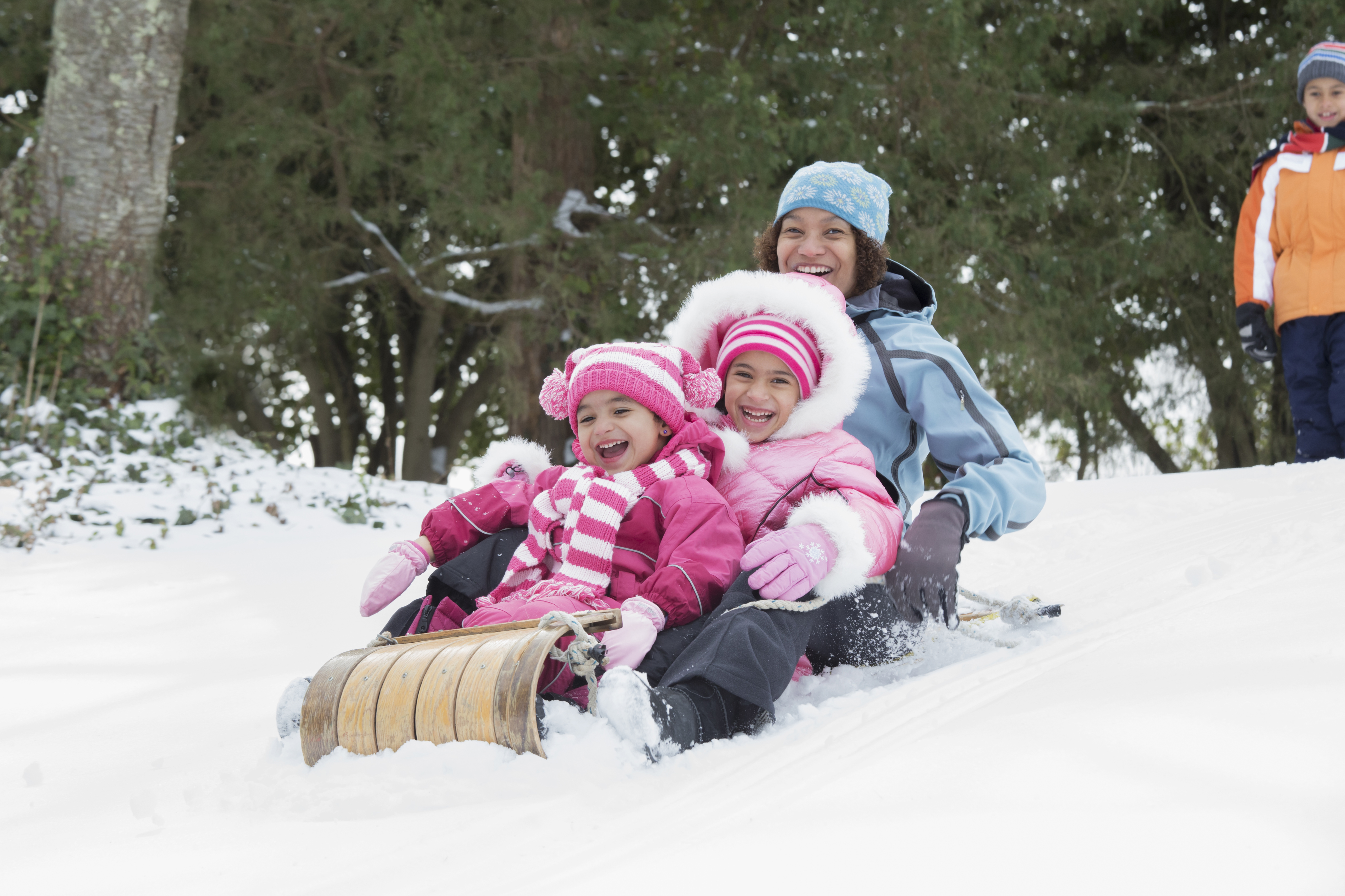 Mother and daughters sledding on snowy hill outdoors