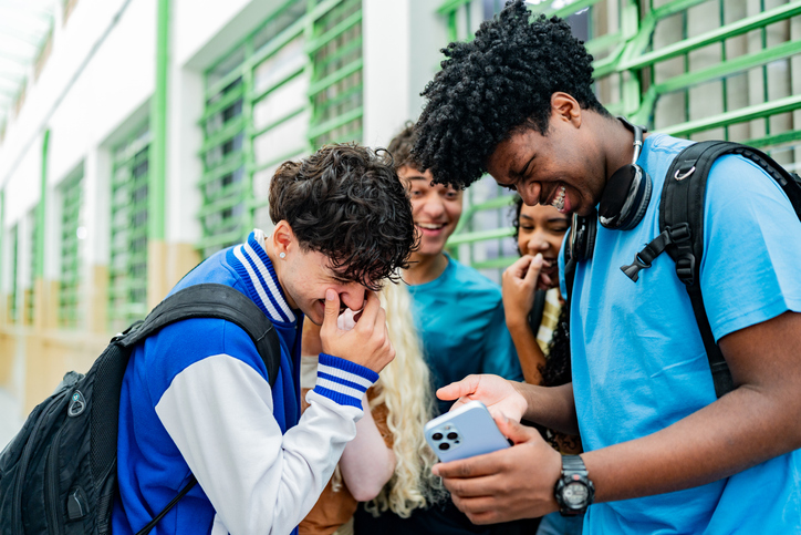 Excited student friends having fun using mobile phone in the school
